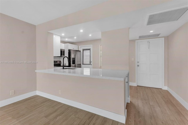 kitchen with appliances with stainless steel finishes, white cabinetry, kitchen peninsula, light wood-type flooring, and sink