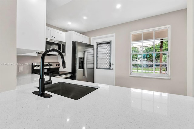 kitchen featuring light stone countertops, white cabinets, appliances with stainless steel finishes, and sink