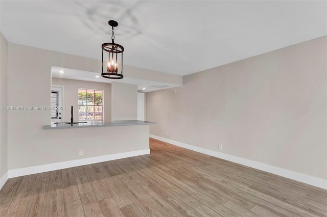 unfurnished living room with light hardwood / wood-style floors, sink, and a notable chandelier