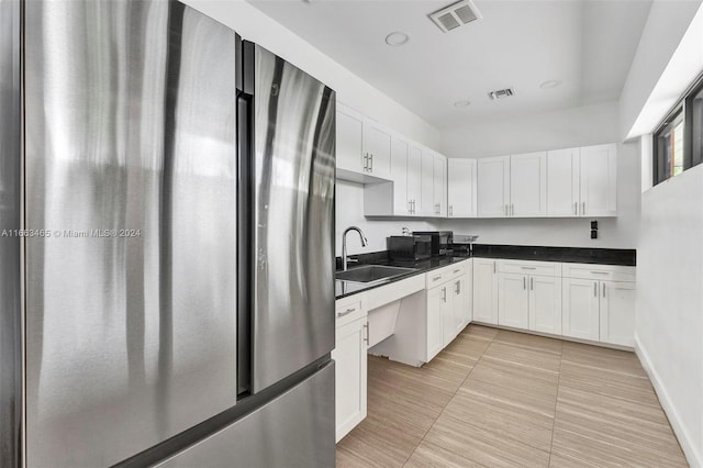 kitchen with white cabinetry, sink, and stainless steel fridge