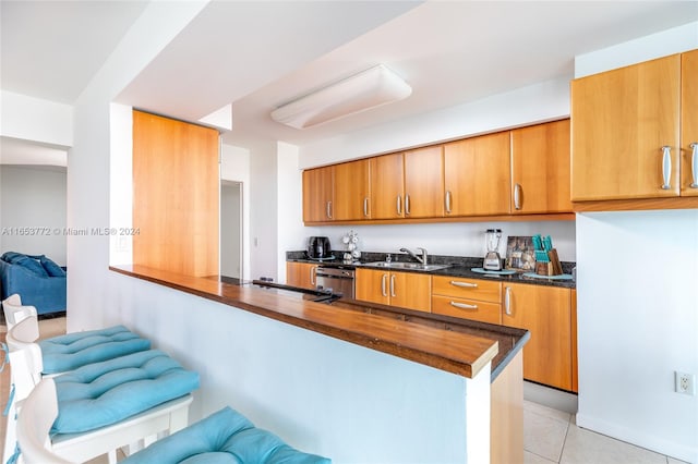 kitchen with dishwasher, sink, kitchen peninsula, light tile patterned floors, and dark stone countertops