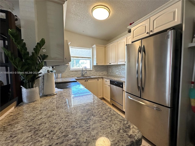 kitchen with backsplash, sink, appliances with stainless steel finishes, light stone counters, and a textured ceiling