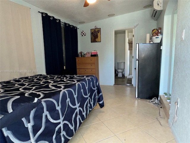 bedroom featuring connected bathroom, an AC wall unit, light tile patterned floors, stainless steel refrigerator, and ceiling fan