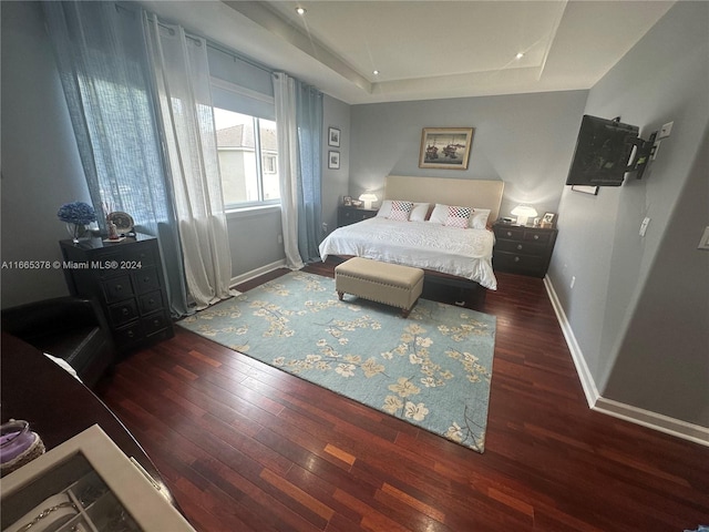 bedroom with a raised ceiling and dark hardwood / wood-style flooring