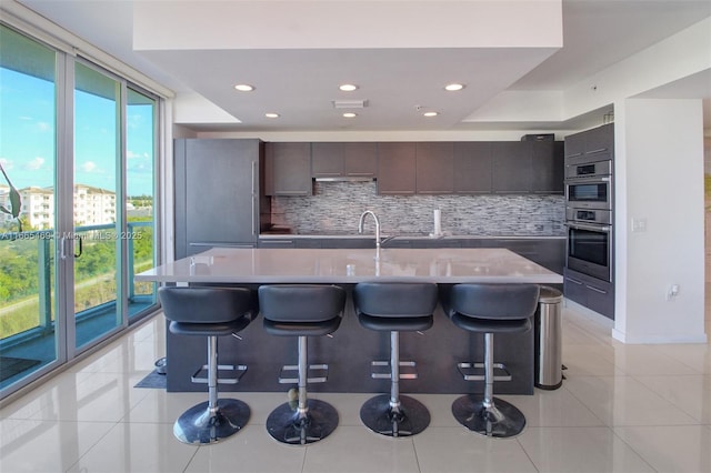 kitchen featuring a kitchen breakfast bar, light tile patterned floors, a center island with sink, and backsplash