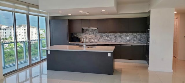 kitchen featuring light tile patterned flooring, backsplash, a kitchen island with sink, and a wealth of natural light