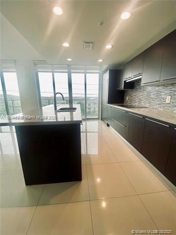 kitchen featuring backsplash, black electric stovetop, sink, and light tile patterned floors