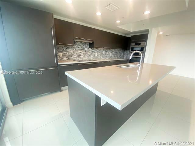 kitchen featuring black electric stovetop, sink, a kitchen island with sink, and light tile patterned floors