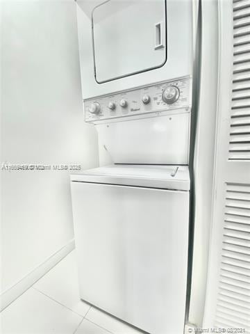 laundry room featuring stacked washer and dryer and light tile patterned floors