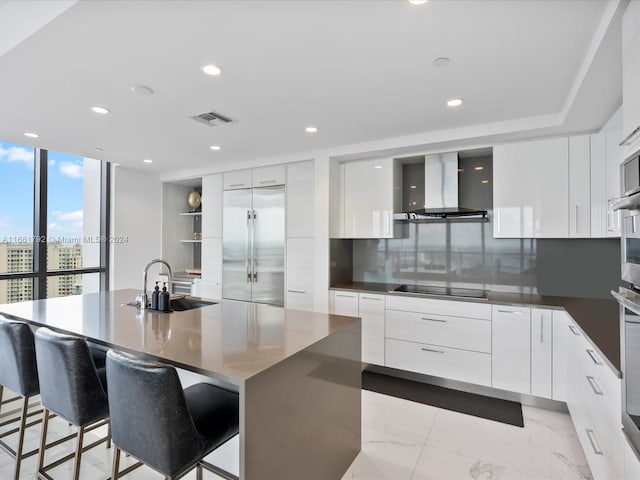 kitchen featuring a large island, sink, white cabinets, wall chimney range hood, and stainless steel appliances