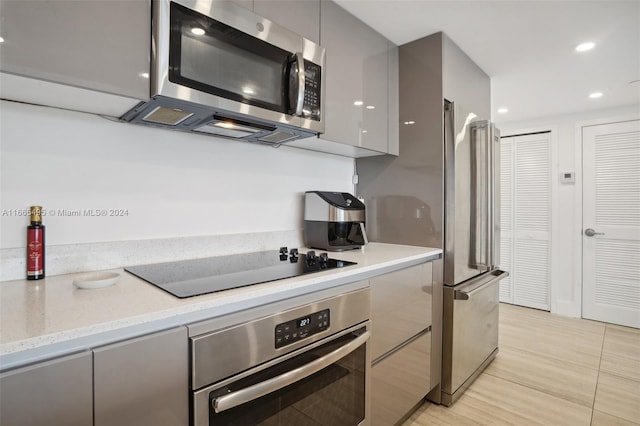 kitchen featuring gray cabinetry, light tile patterned floors, appliances with stainless steel finishes, and light stone countertops