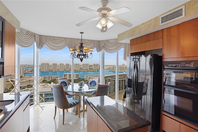 kitchen featuring ceiling fan with notable chandelier, hanging light fixtures, black appliances, a water view, and dark stone countertops