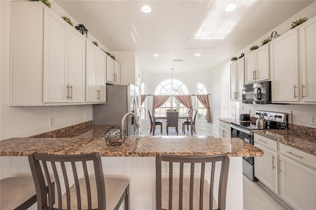 kitchen featuring kitchen peninsula, appliances with stainless steel finishes, a kitchen breakfast bar, pendant lighting, and dark stone countertops