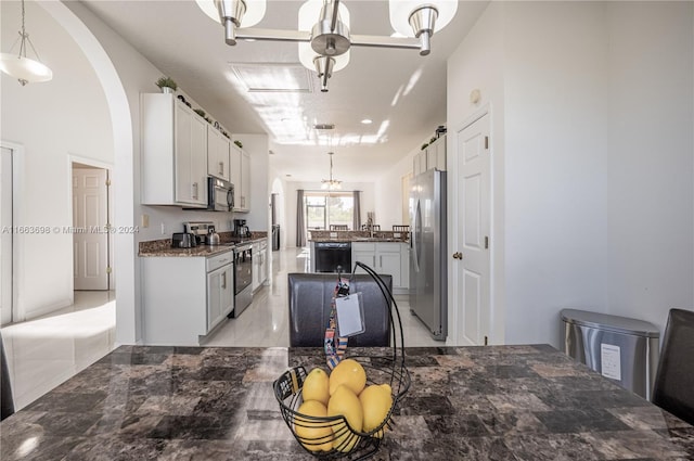 kitchen with appliances with stainless steel finishes, white cabinetry, pendant lighting, and dark stone countertops