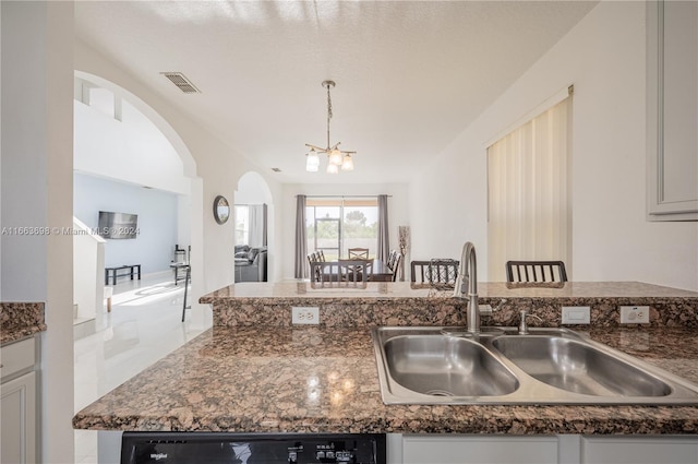 kitchen featuring dishwasher, sink, dark stone counters, pendant lighting, and a chandelier