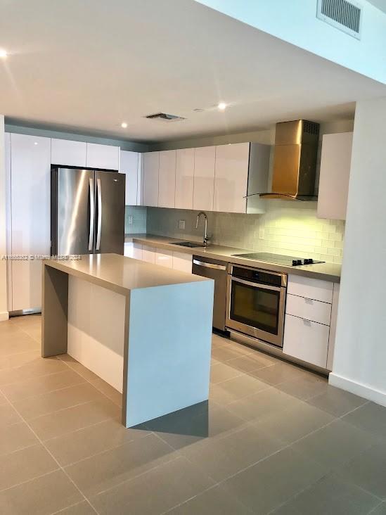 kitchen with white cabinetry, a kitchen island, stainless steel appliances, sink, and wall chimney range hood