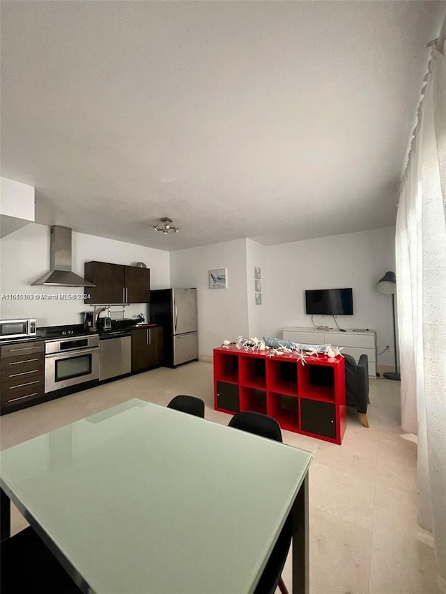 kitchen with appliances with stainless steel finishes, dark brown cabinets, and wall chimney range hood