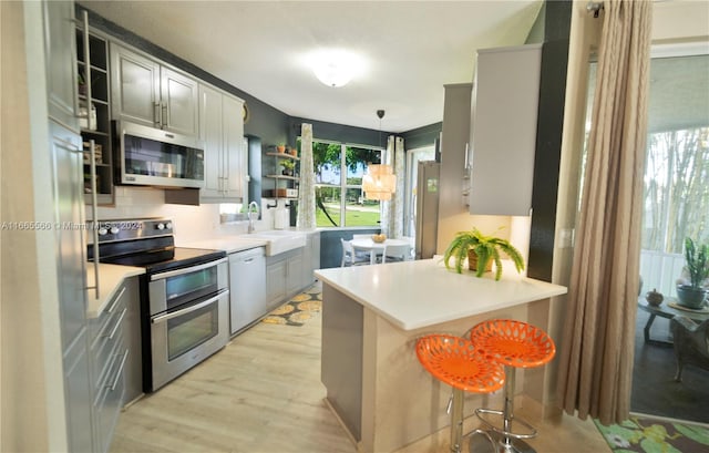 kitchen featuring gray cabinets, sink, a kitchen bar, appliances with stainless steel finishes, and decorative light fixtures