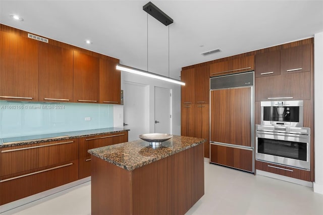 kitchen with hanging light fixtures, dark stone countertops, a kitchen island, paneled refrigerator, and double oven