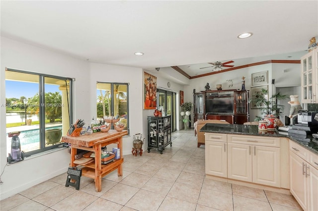 kitchen featuring dark stone counters, ceiling fan, light tile patterned flooring, and crown molding