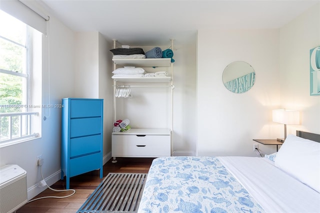 bedroom with multiple windows, dark wood-type flooring, and a wall unit AC