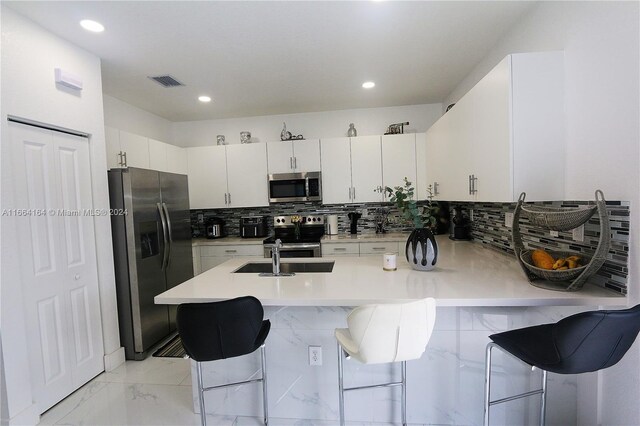 kitchen featuring a kitchen breakfast bar, tasteful backsplash, white cabinets, stainless steel appliances, and sink