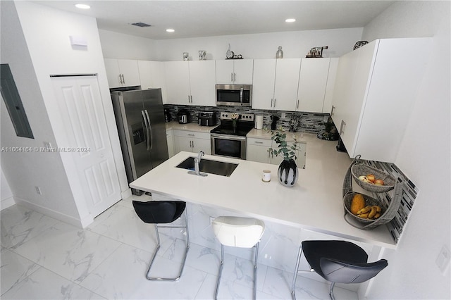 kitchen featuring sink, kitchen peninsula, white cabinetry, stainless steel appliances, and a kitchen bar