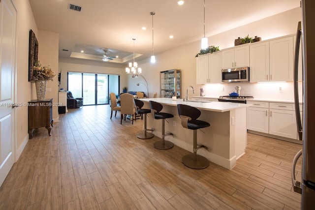 kitchen featuring light hardwood / wood-style flooring, a center island with sink, hanging light fixtures, white cabinets, and appliances with stainless steel finishes