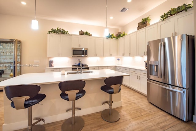 kitchen with light wood-type flooring, a kitchen island with sink, stainless steel appliances, white cabinets, and pendant lighting