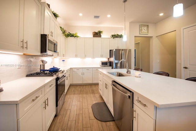 kitchen featuring sink, decorative light fixtures, a center island with sink, white cabinetry, and appliances with stainless steel finishes