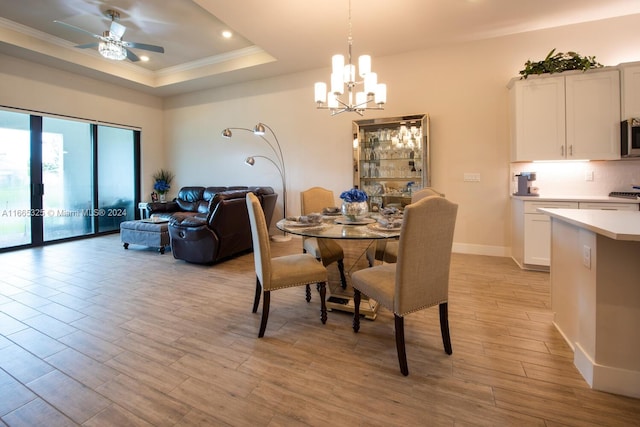 dining room with ceiling fan with notable chandelier, light wood-type flooring, crown molding, and a tray ceiling