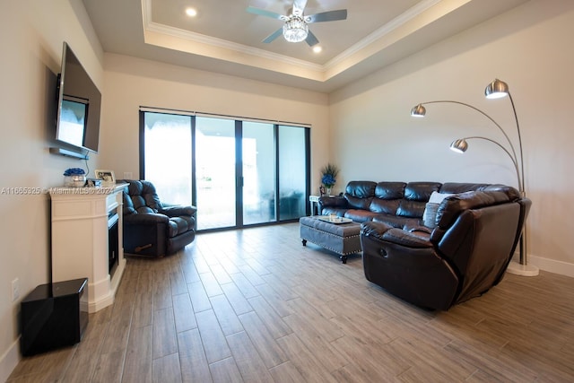 living room featuring a raised ceiling, ornamental molding, light hardwood / wood-style flooring, and ceiling fan