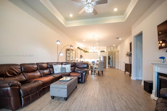 living room featuring ceiling fan with notable chandelier, light hardwood / wood-style floors, crown molding, and a tray ceiling