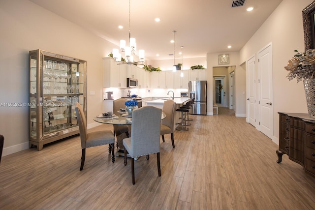 dining space featuring light wood-type flooring, sink, and an inviting chandelier