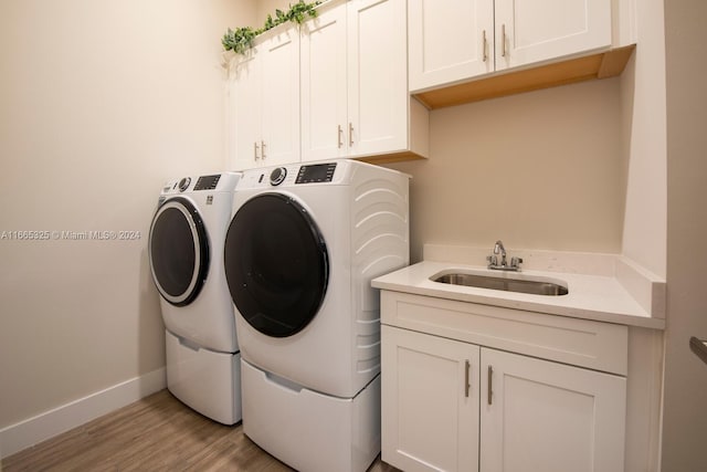 laundry area featuring washing machine and clothes dryer, cabinets, sink, and light wood-type flooring