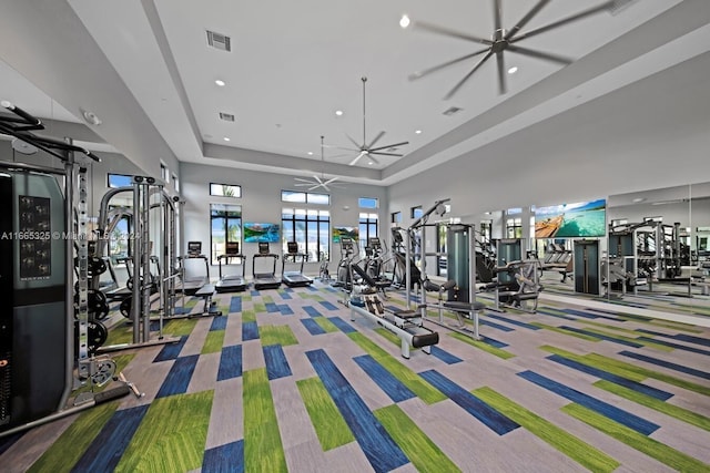 exercise room featuring a towering ceiling, a tray ceiling, carpet, and ceiling fan