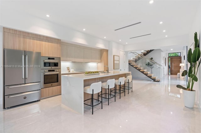 kitchen with a kitchen island with sink, sink, a breakfast bar area, light brown cabinets, and appliances with stainless steel finishes