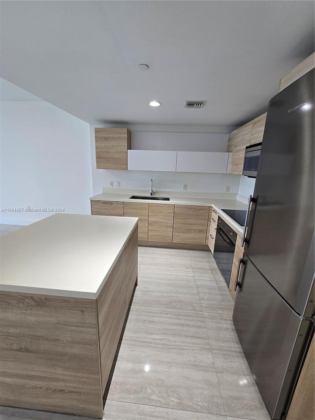 kitchen with sink, light brown cabinetry, black appliances, and a center island