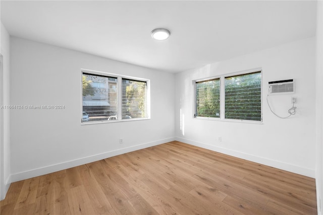 empty room with a wall unit AC, light hardwood / wood-style flooring, and a wealth of natural light