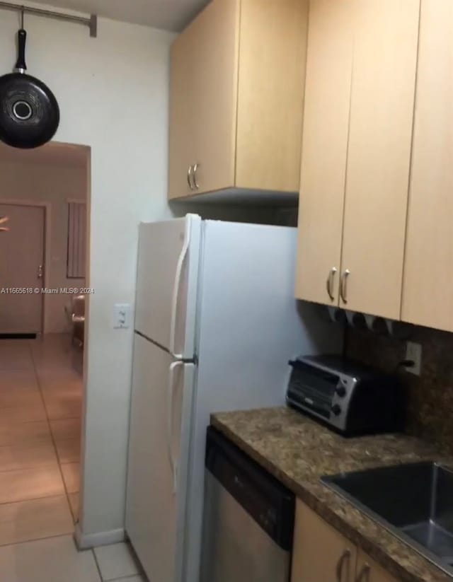 kitchen featuring dark stone counters, cream cabinetry, light tile patterned floors, and stainless steel dishwasher