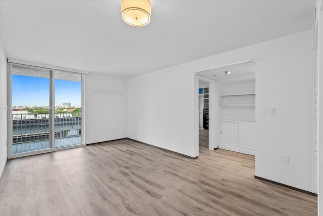 spare room with light wood-type flooring, built in features, and floor to ceiling windows