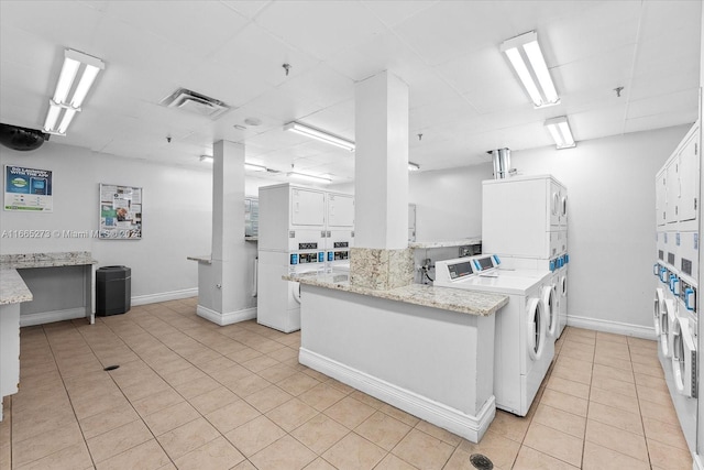 kitchen featuring light stone counters, light tile patterned flooring, stacked washer and clothes dryer, white cabinetry, and washing machine and dryer