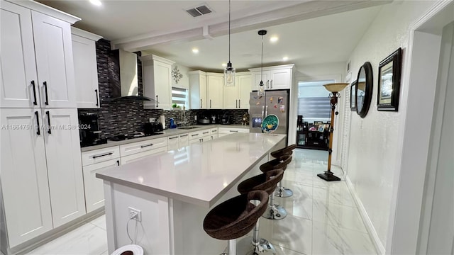 kitchen with a kitchen bar, stainless steel refrigerator with ice dispenser, wall chimney range hood, a kitchen island, and pendant lighting