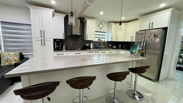 kitchen featuring decorative backsplash, a breakfast bar, white cabinetry, decorative light fixtures, and stainless steel fridge