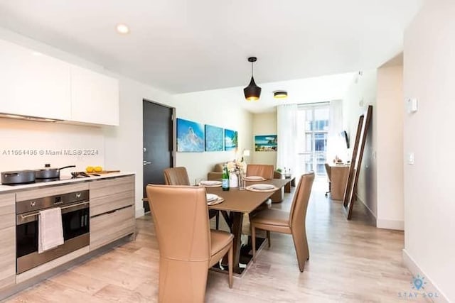 kitchen featuring light wood-type flooring, white cabinetry, oven, and hanging light fixtures