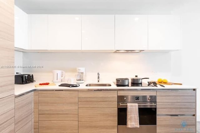 kitchen featuring sink, oven, cooktop, and white cabinetry