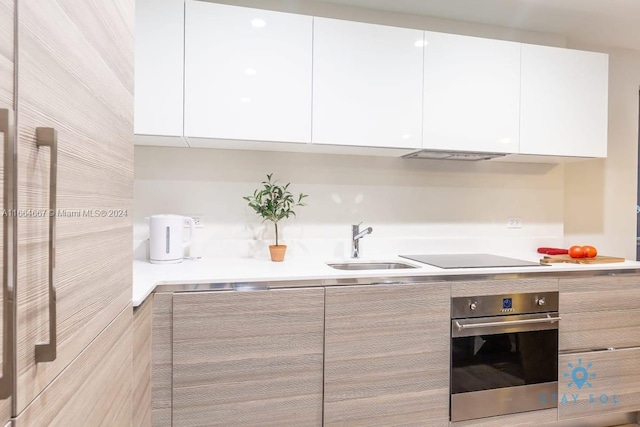 kitchen with black electric cooktop, white cabinets, sink, and stainless steel oven