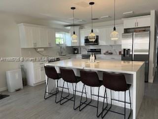 kitchen with white cabinetry, a breakfast bar, stainless steel appliances, a center island, and decorative light fixtures