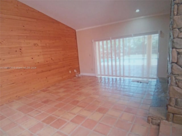 tiled empty room with wood walls, crown molding, and vaulted ceiling