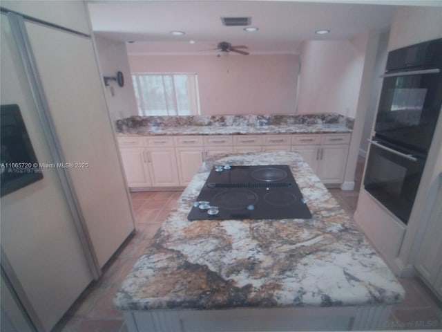 kitchen featuring white cabinetry, a center island, ceiling fan, light stone countertops, and black appliances